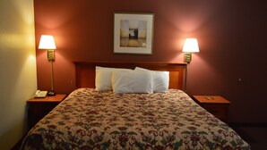 Une chambre d’hôtel avec une couvre-lit à motifs floraux, deux lampes de chevet, un tableau encadré au mur et une tête de lit en bois.