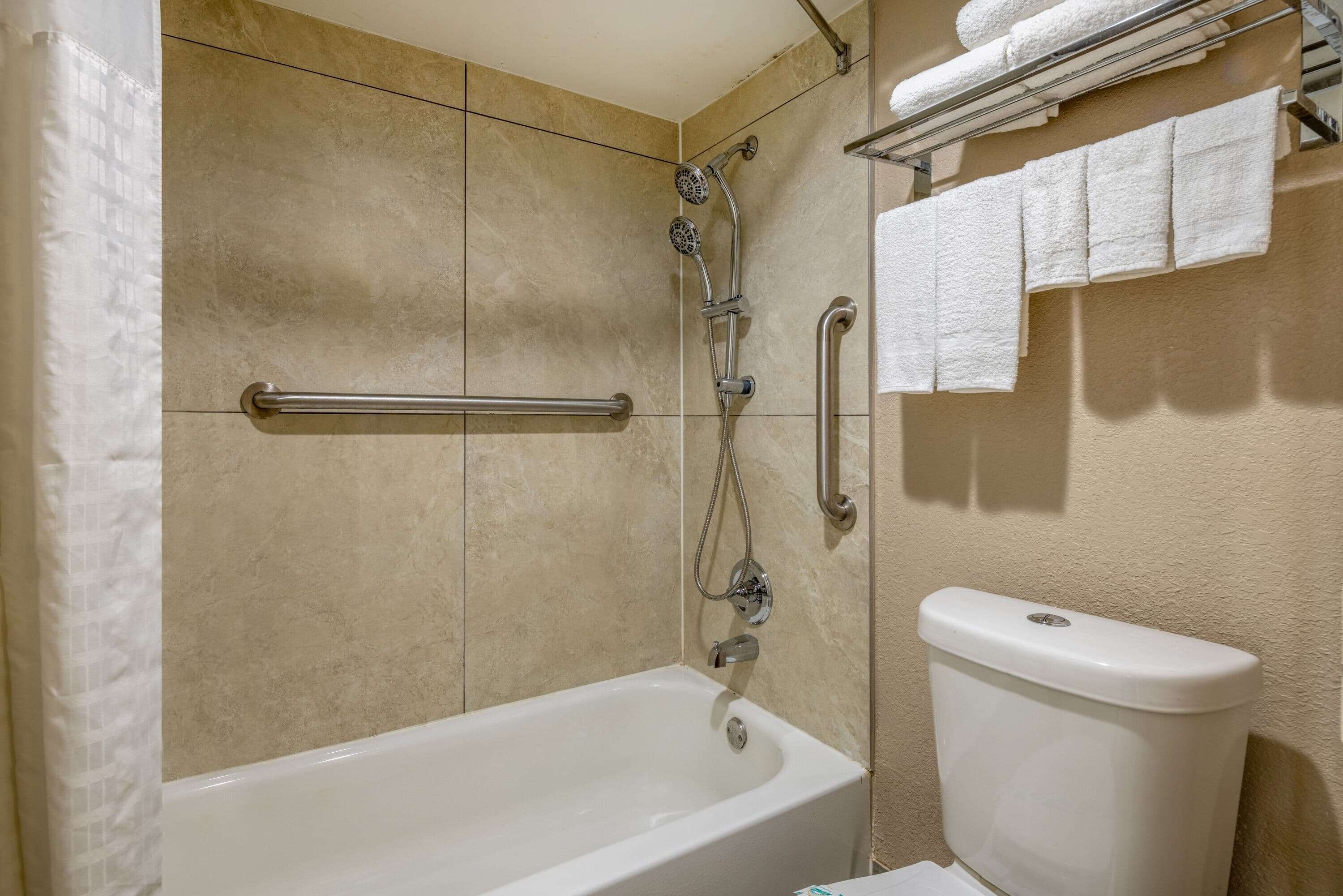 Une salle de bain équipée d’une baignoire, d’une douche et de toilettes. On y trouve un porte-serviettes avec des serviettes et une barre d’appui.