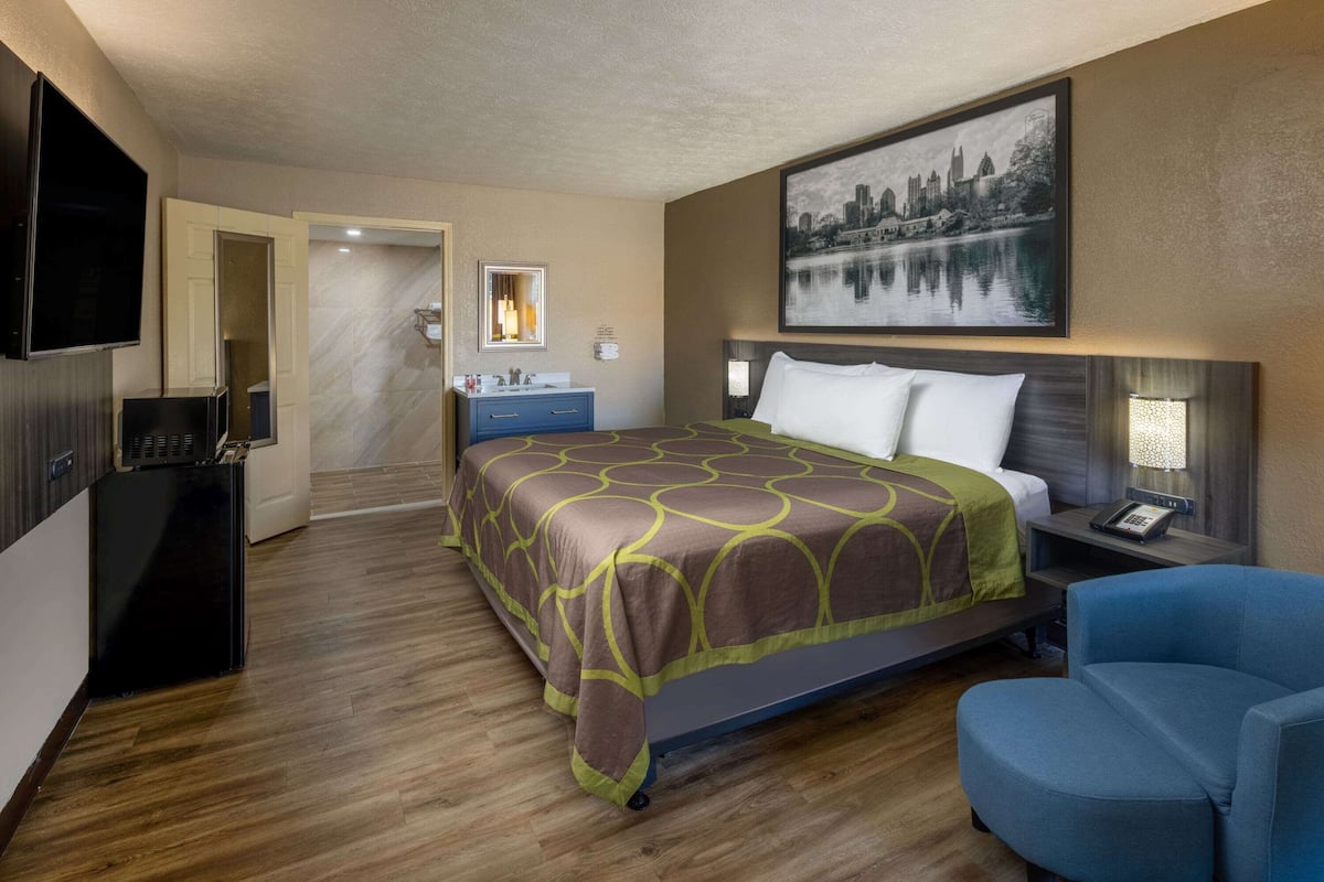 Une chambre d’hôtel avec un lit, un bureau, une chaise, une télévision et un tableau au mur.