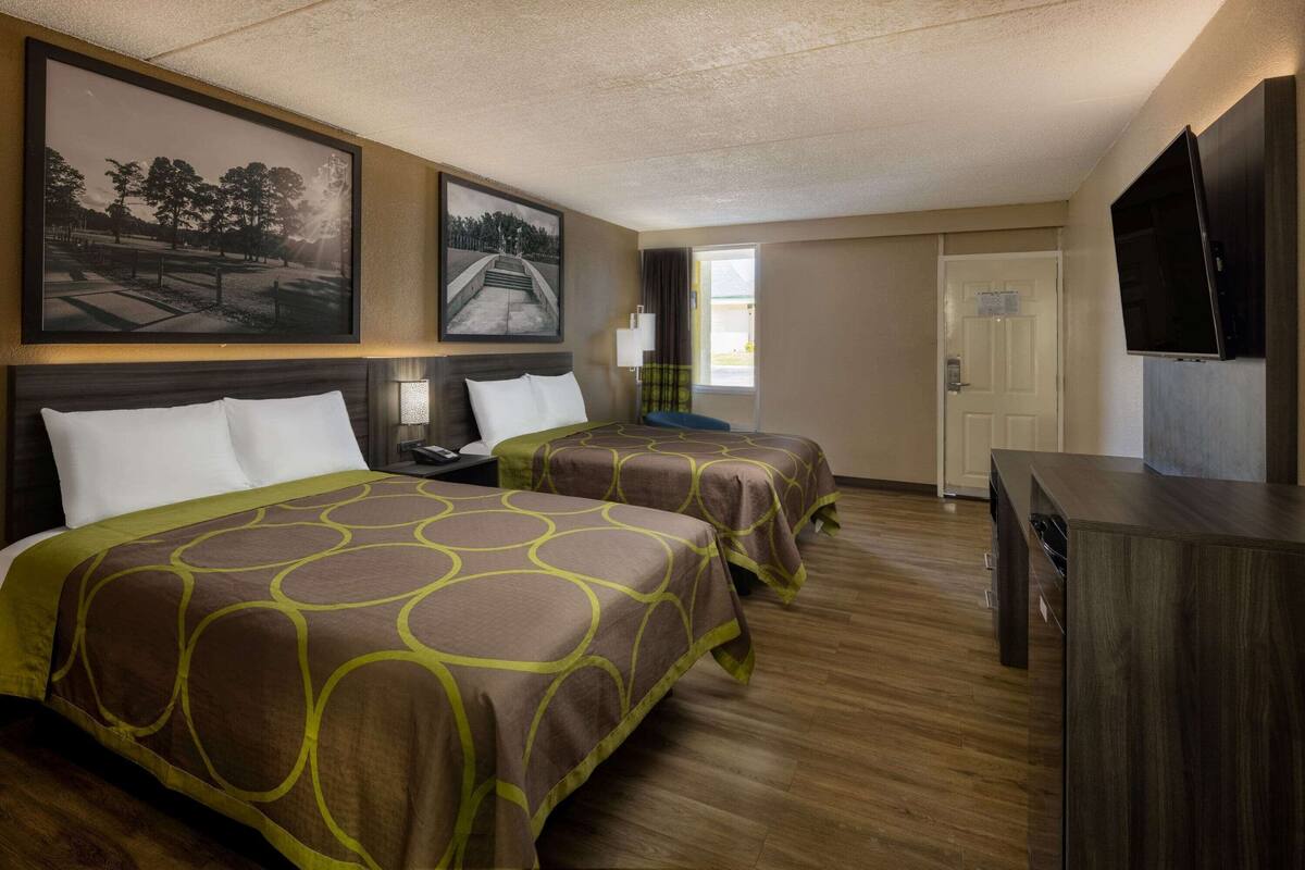 Une chambre d’hôtel avec deux lits, une télévision, un bureau et une fenêtre donnant sur l’extérieur.
