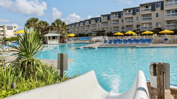 A swimming pool with lounge chairs and umbrellas, surrounded by a multi-story building with balconies. - A Place at the Beach (Atlantic Beach)