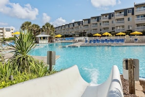 A swimming pool with lounge chairs and umbrellas, surrounded by a multi-story building with balconies. - A Place at the Beach (Atlantic Beach)