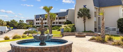 A hotel with a fountain, palm trees, and a parking lot.