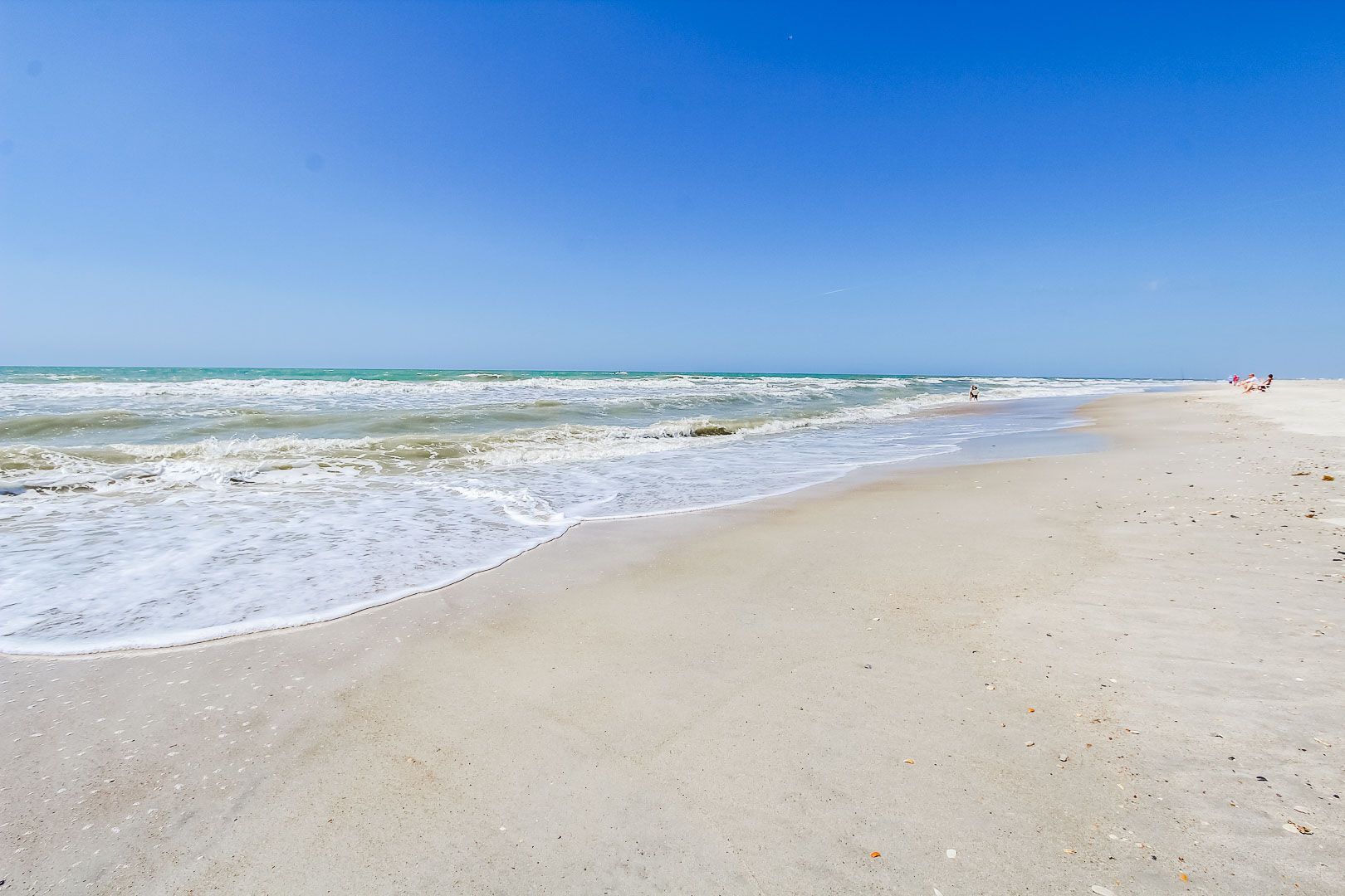 A beach with waves, a clear sky, and a few people in the distance.