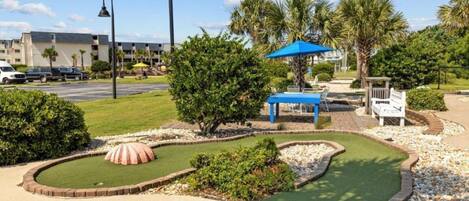 A miniature golf course with a putting green, sand bunkers, and a blue umbrella.