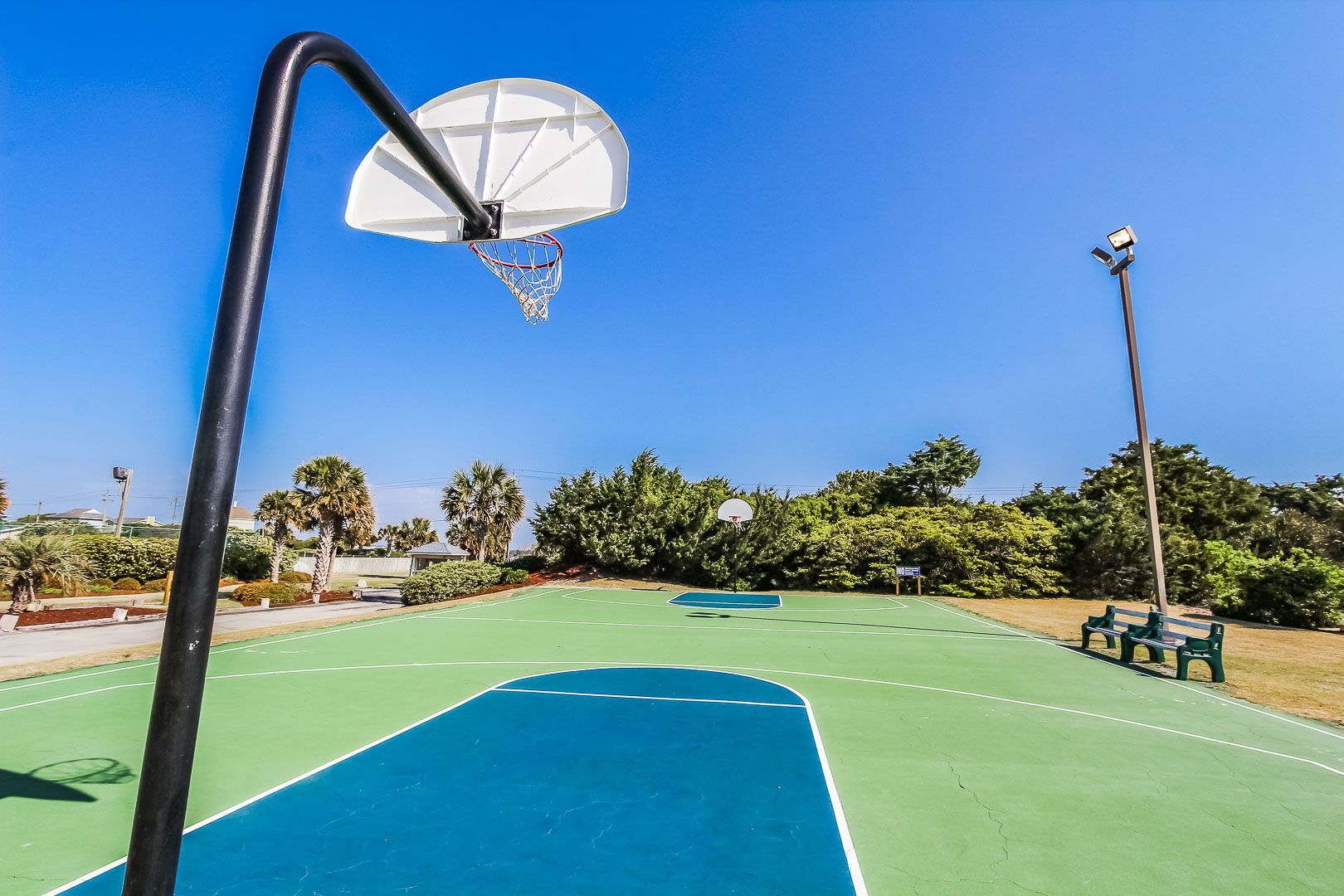 Una cancha de baloncesto al aire libre con aro, bancos y cielo despejado.