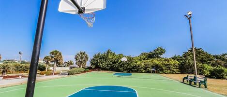 An outdoor basketball court with a hoop, benches, and a clear sky.