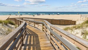 A wooden boardwalk leading to a sandy beach with umbrellas and people. - A Place at the Beach (Atlantic Beach)