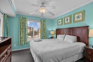 A bedroom with a bed, a nightstand, a lamp, a ceiling fan, and a window with curtains. - A Place at the Beach (Atlantic Beach)