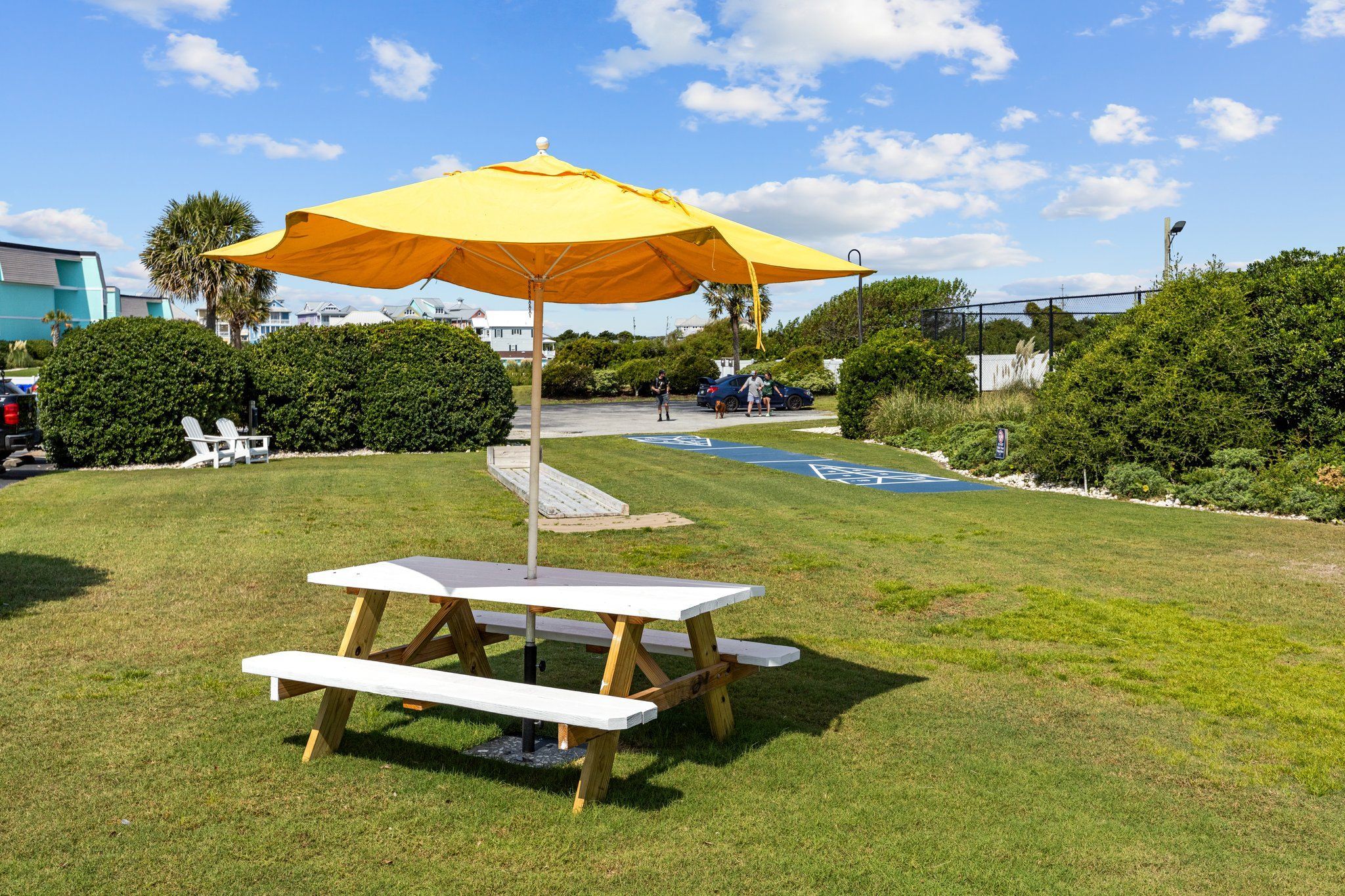 A picnic table with a yellow umbrella, surrounded by grass and bushes.
