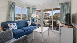 A modern hotel room with a blue sofa, a small table, and a balcony with a view of the city. - A Place at the Beach (Atlantic Beach)
