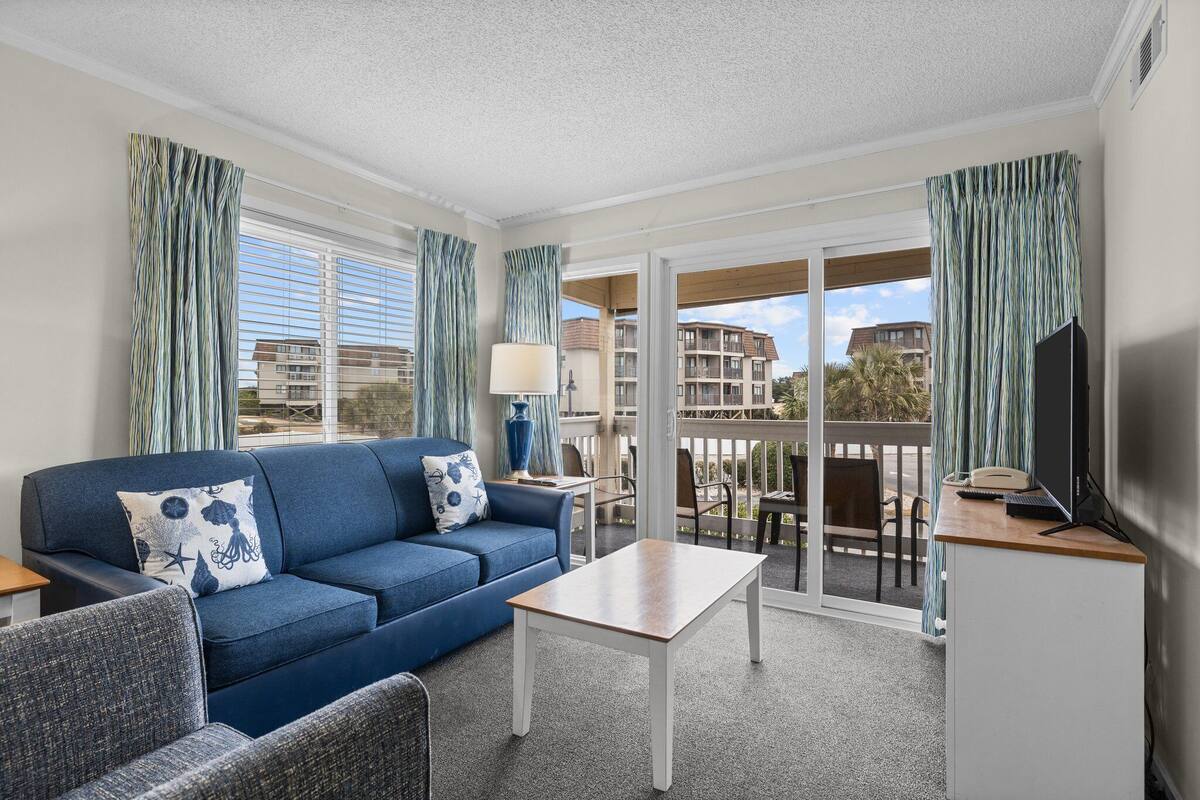 Una habitación de hotel moderna con un sofá azul, una mesita y un balcón con vistas a la ciudad.