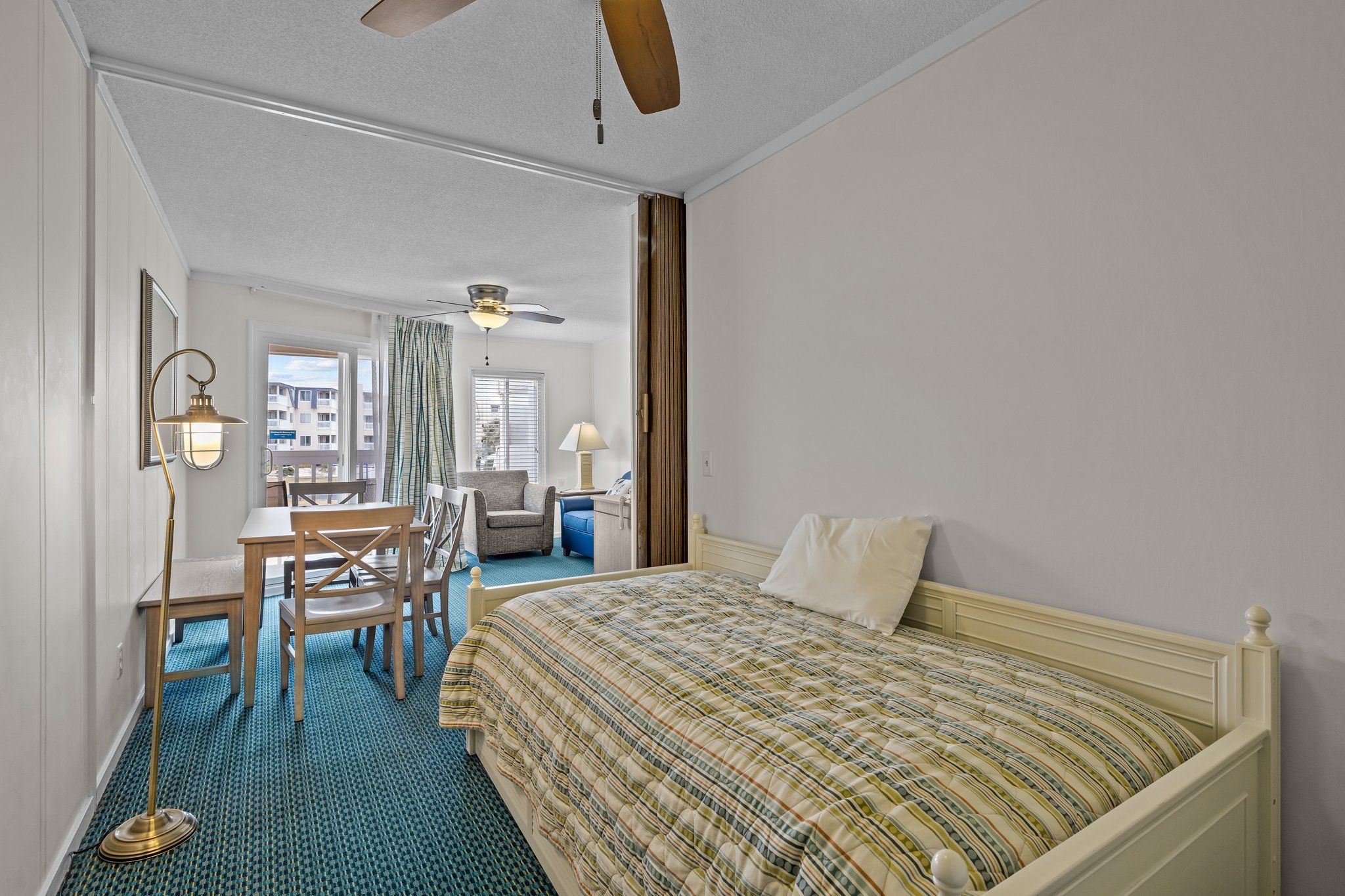 A hotel room with a bed, a desk, and a chair. There is a ceiling fan and a window with curtains.