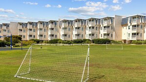 Un but de football sur un terrain herbeux, avec une rangée d’immeubles d’habitation en arrière-plan.