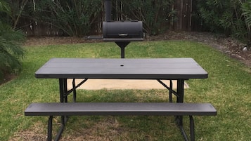 A picnic table with a barbecue grill in a backyard.