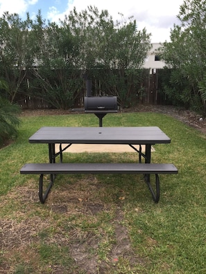 A picnic table with a barbecue grill in a backyard.