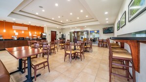 Un grand espace de salle à manger avec plusieurs tables et chaises, un coin cuisine équipé d’appareils électroménagers et un téléviseur fixé au mur.