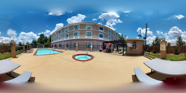 A hotel with a swimming pool, outdoor seating, and a covered patio area.