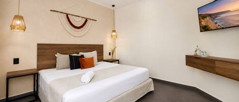 A modern hotel room with a large bed, two bedside tables, a wall-mounted TV, and a decorative wall hanging.