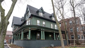 A large, two-story house with a wrap-around porch, brick exterior, and multiple windows.