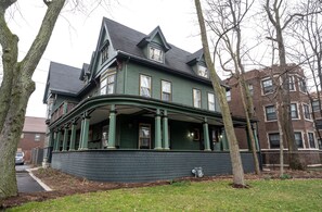 A large, two-story house with a wrap-around porch, brick exterior, and multiple windows.