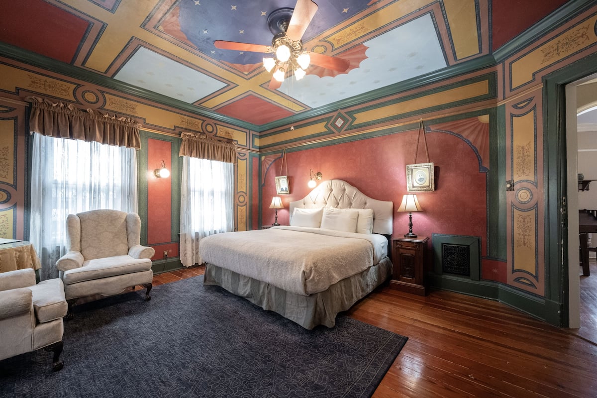 A bedroom with a large bed, two bedside tables, a chair, and a ceiling fan.