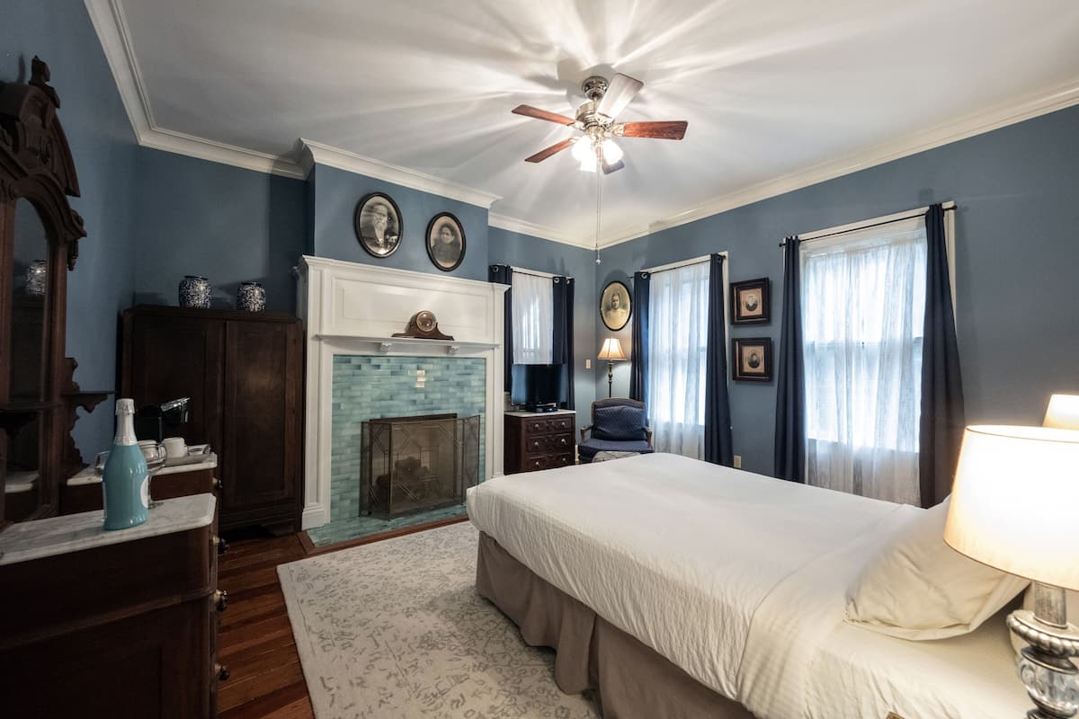 A bedroom with a large bed, a ceiling fan, a fireplace, and a television.