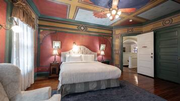 A room with a large bed, a chair, a ceiling fan, and a door.
