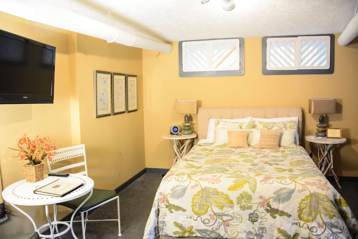 A hotel room with a bed, two bedside tables, a chair, a TV, and framed pictures on the wall.