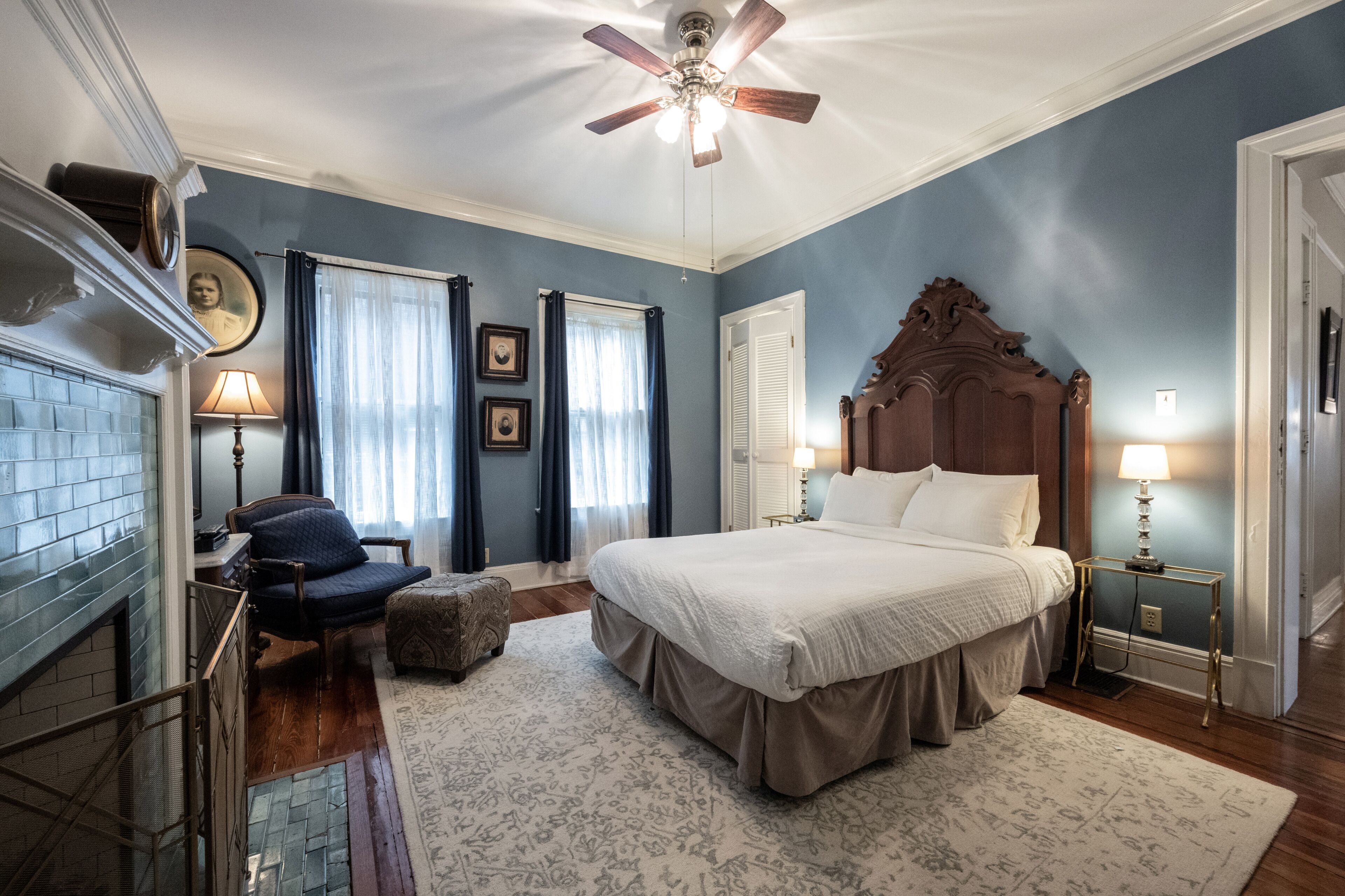 Une chambre avec un grand lit, un ventilateur de plafond, une cheminée et un fauteuil.