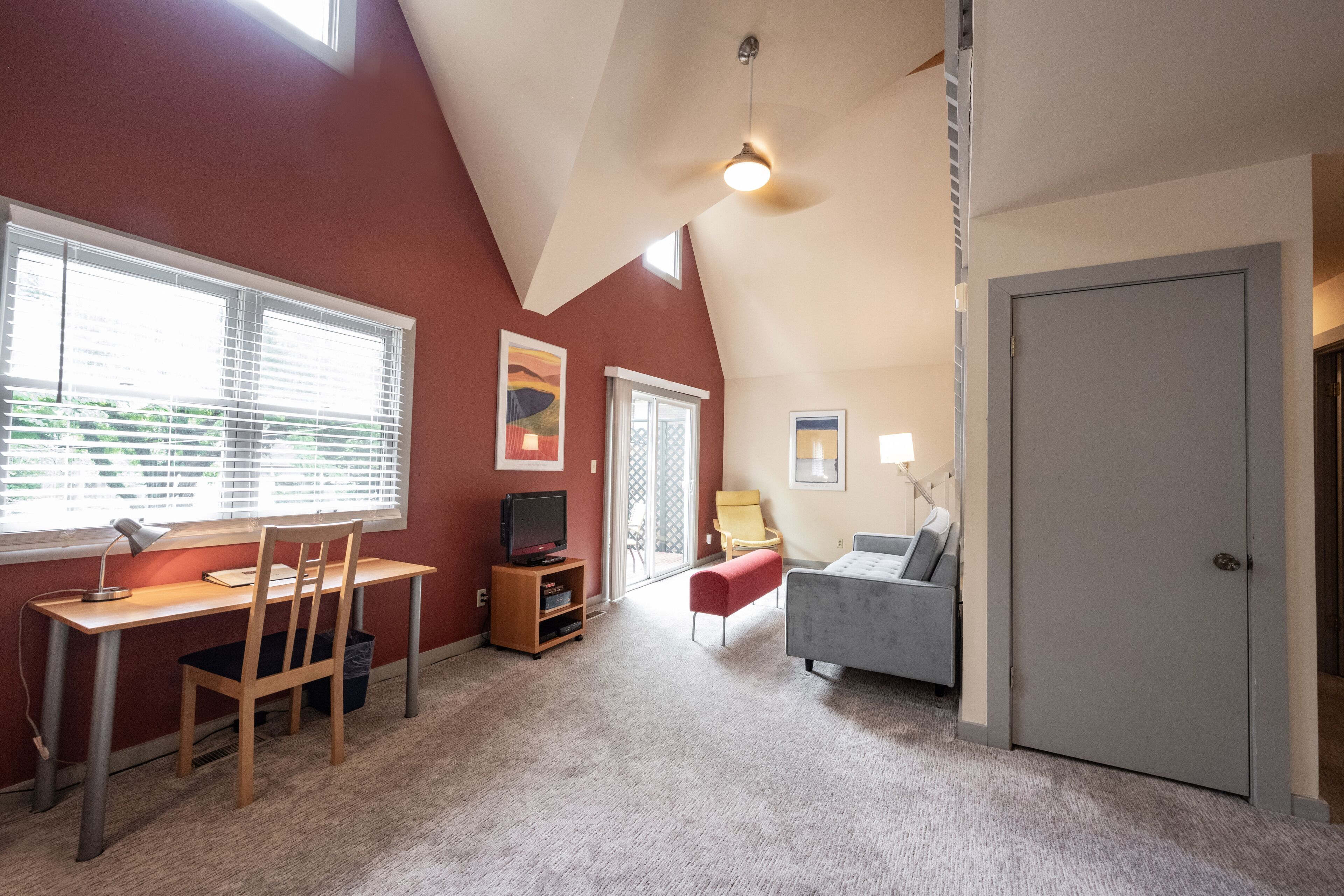 A room with a sloped ceiling, a desk with a chair, a couch, and a door.