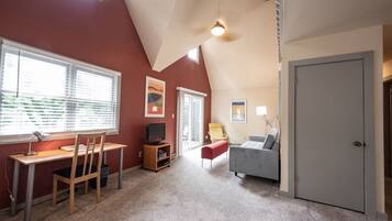 A room with a sloped ceiling, a desk with a chair, a couch, and a door.