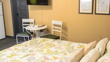 Un dormitorio con una colcha estampada, dos sillas, una mesita redonda, un televisor y dos cuadros en la pared.