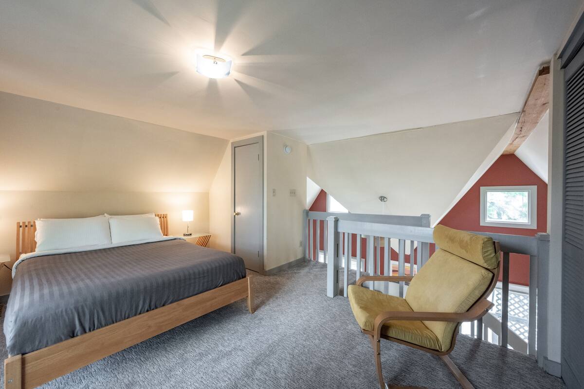 A bedroom with a bed, a chair, and a balcony.