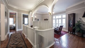 A spacious foyer with a high ceiling, white railings, and a patterned rug leading to a staircase.