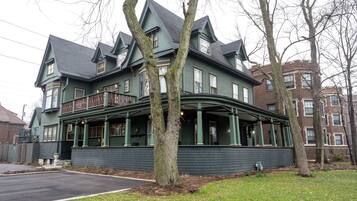 A large, green Victorian-style building with a curved balcony, multiple windows, and a brick facade.