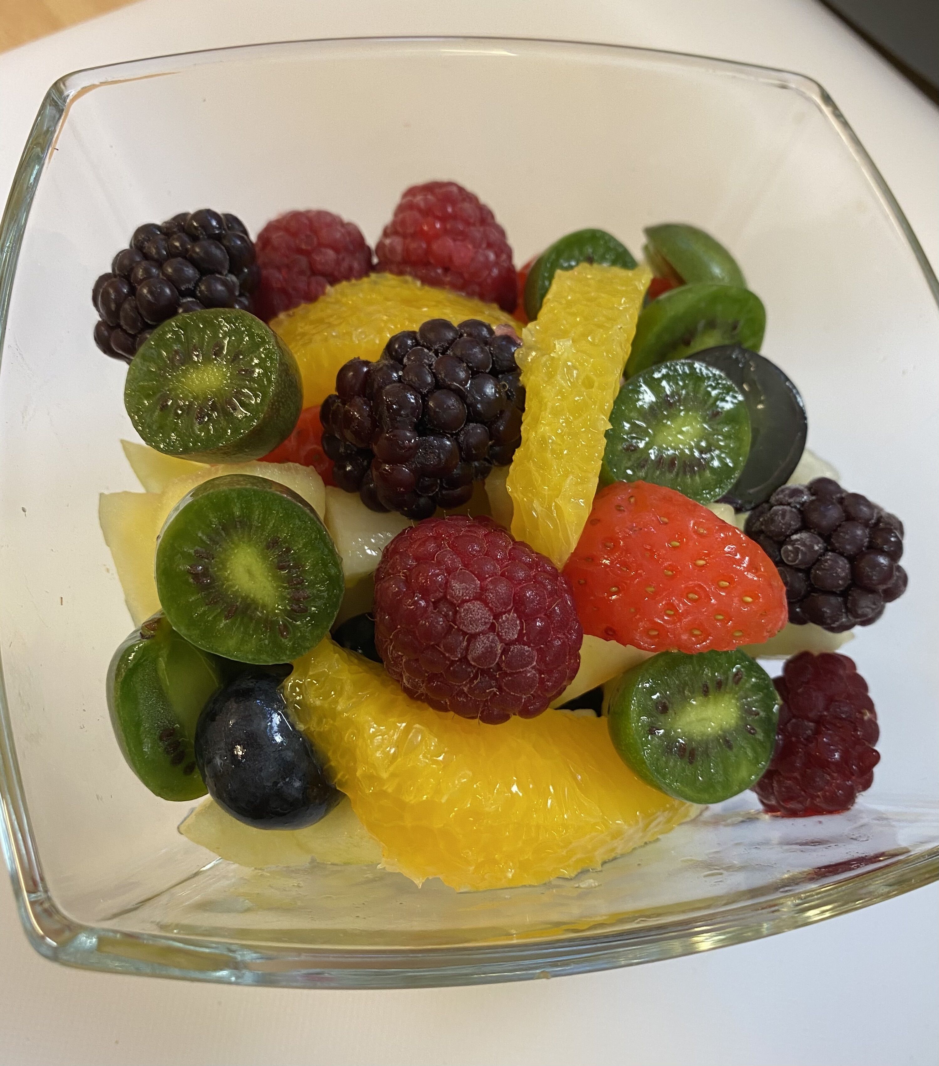 A glass bowl filled with assorted fruits including kiwi, strawberries, blackberries, and grapes.