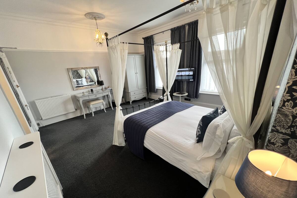 Ein Hotelzimmer mit Bett, Schreibtisch, Stuhl, Spiegel, Heizkörper und einem Fenster mit Vorhängen.