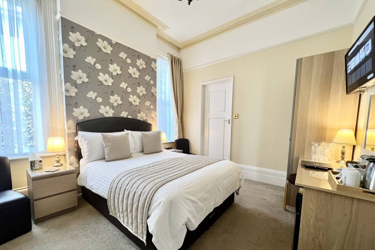 Ein Hotelzimmer mit Bett, Nachttischen, Schreibtisch, Stuhl, Fernseher und einem Fenster mit Vorhängen.