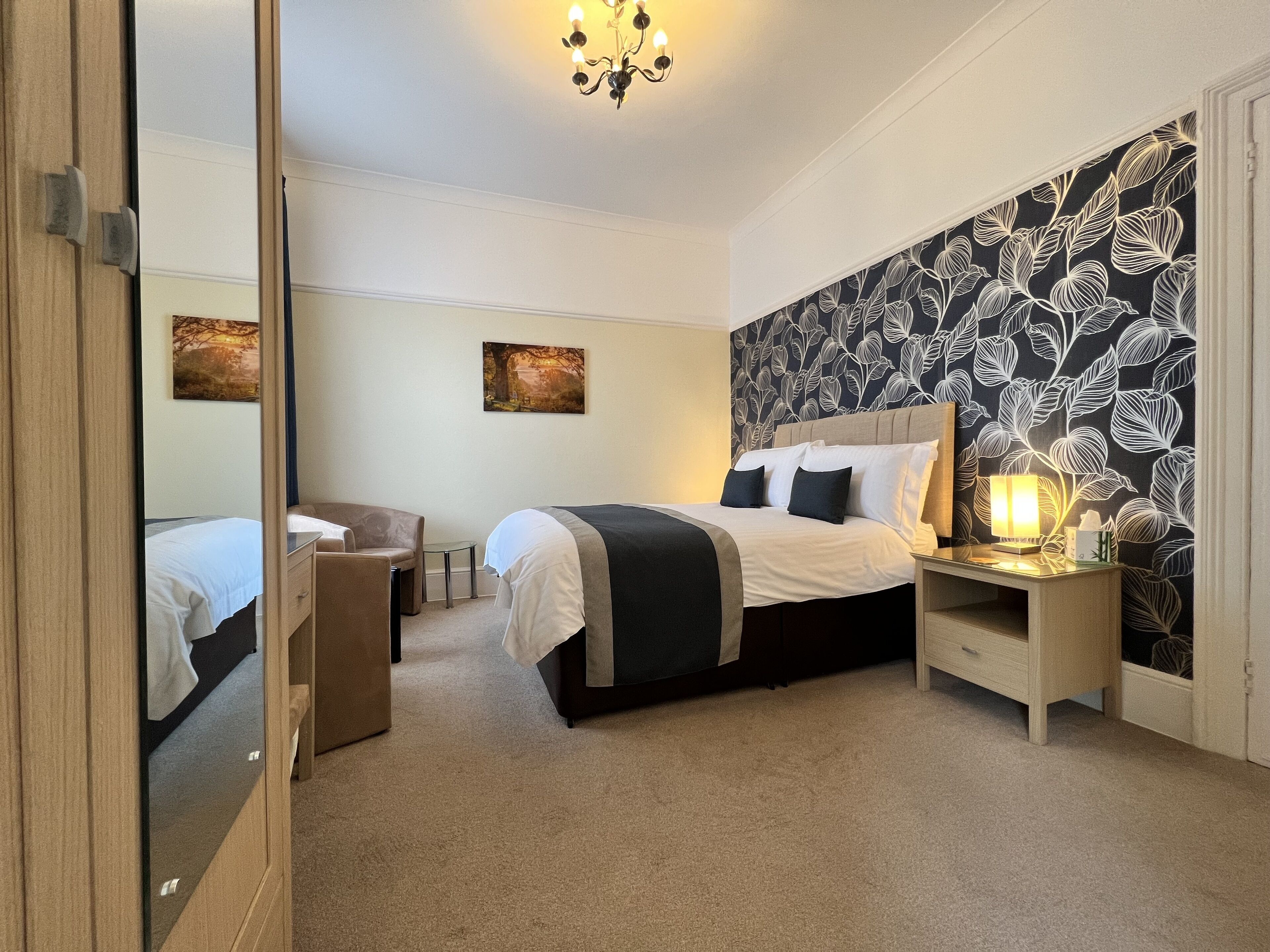 A bedroom with a bed, bedside table, lamp, and a mirror.
