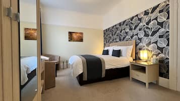 A bedroom with a bed, bedside table, lamp, and a mirror.