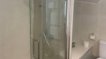 Een douche met glazen wand, een handdouche, toilet en een klein plankje met een rol toiletpapier.