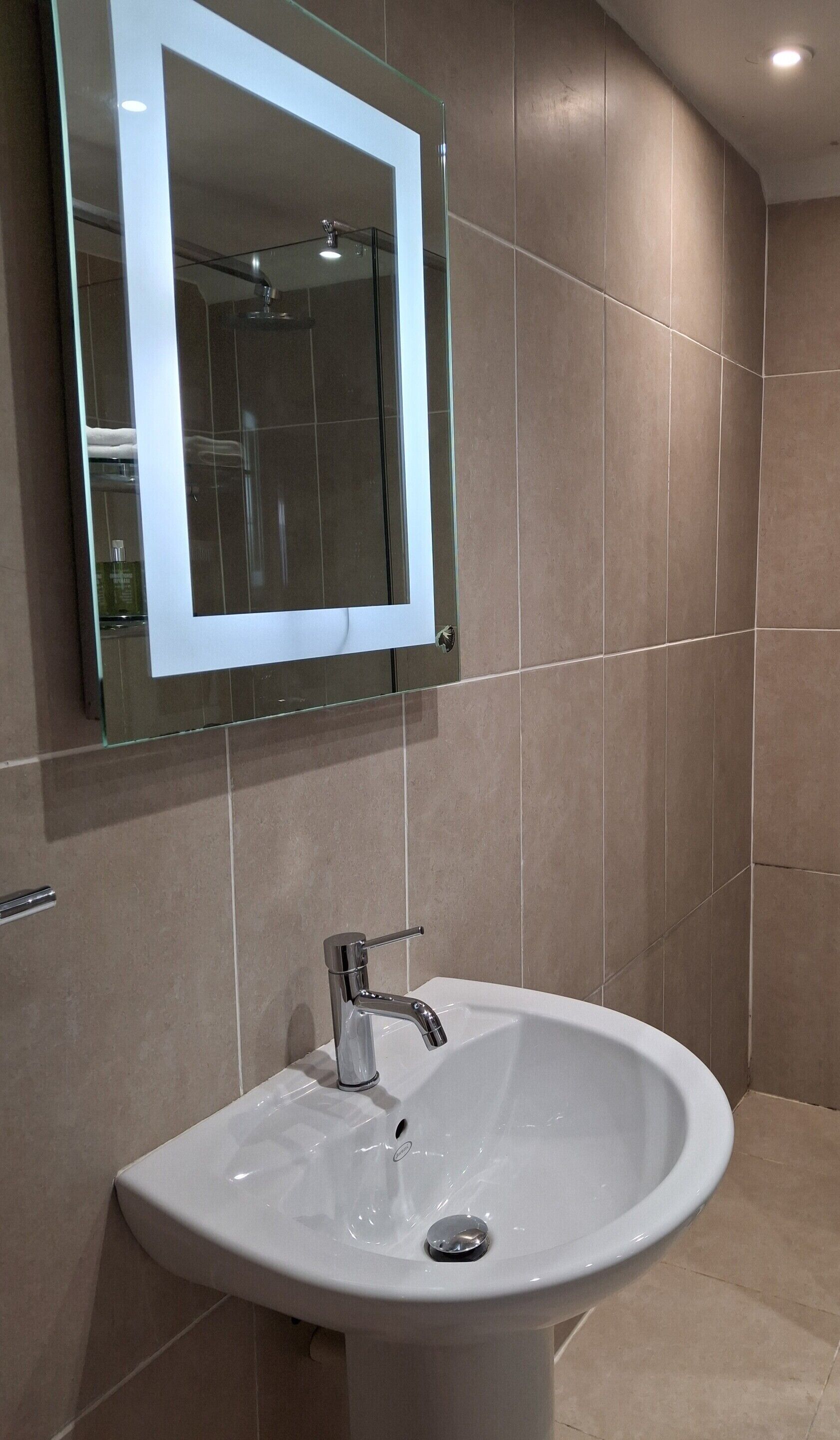 A bathroom with a white sink, chrome faucet, and a glass-framed mirror.
