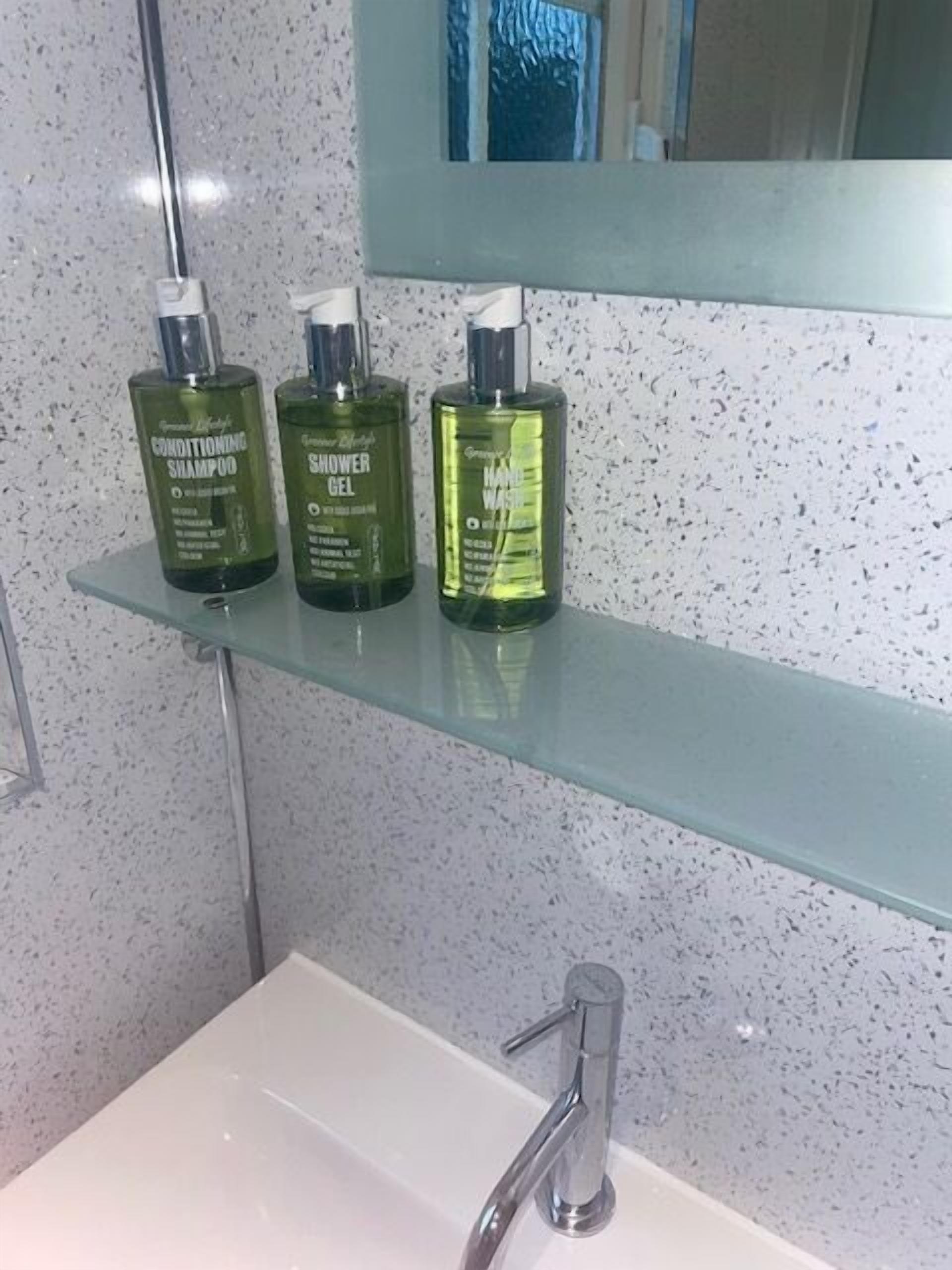 Un baño con un estante de vidrio que sostiene tres productos de cuidado personal.