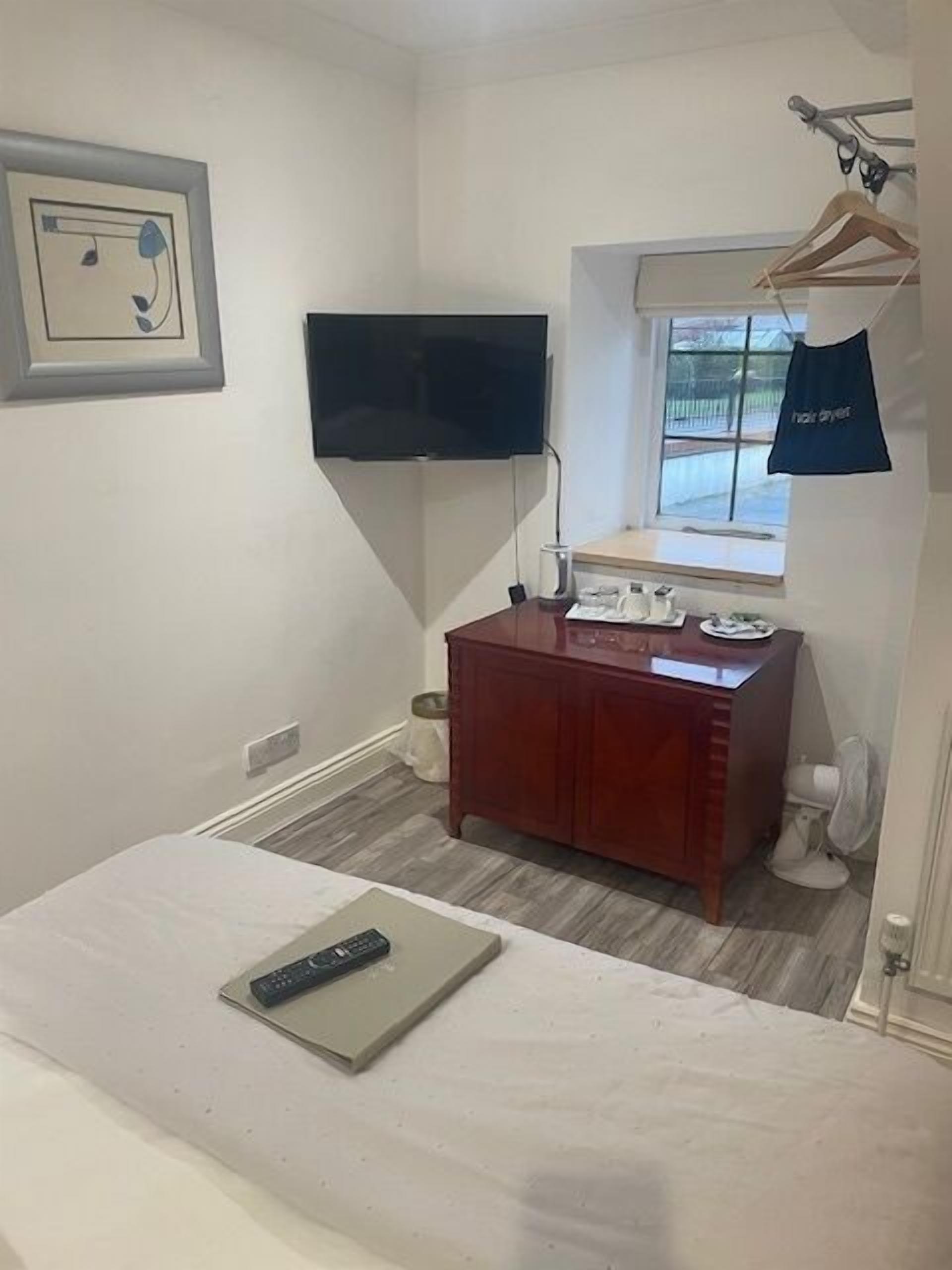 A bedroom with a bed, a dresser, a TV mounted on the wall, and a window with a view.