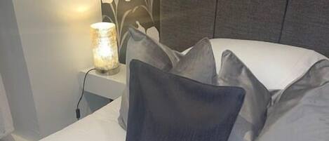 A neatly made bed with a white sheet, a dark gray pillow, and a light gray pillow.