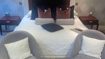 A hotel room with a large bed, two armchairs, a wooden headboard, and wall-mounted lamps.