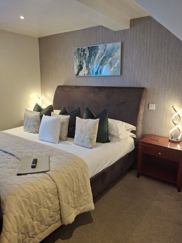A neatly made bed with a quilt, pillows, and a remote control on it. There is a nightstand with a lamp and a power outlet. - La Fontana Italian Restaurant With Rooms (Wantage)