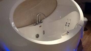 A modern, oval-shaped bathtub with a built-in seat and a handheld showerhead.