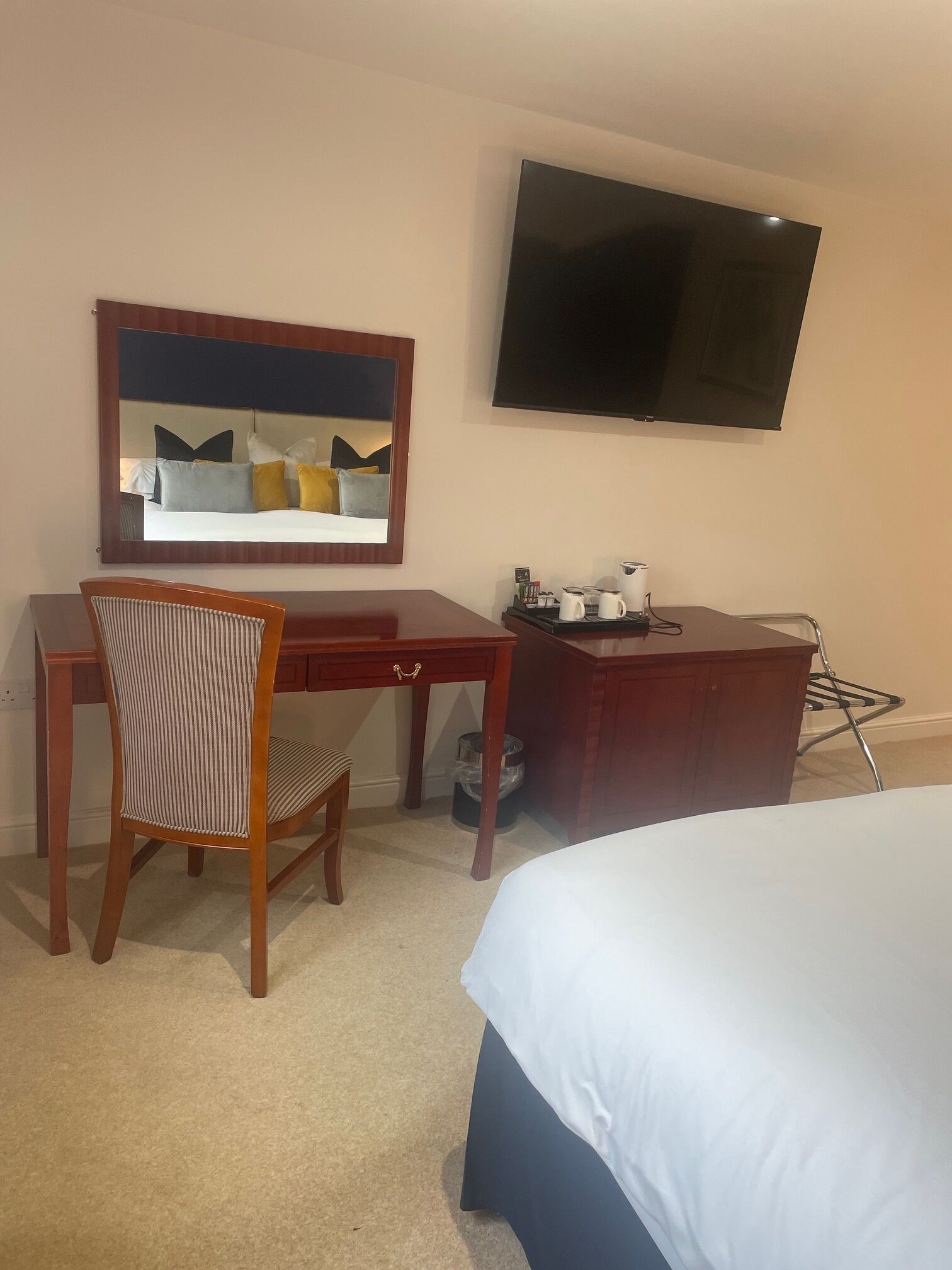 A hotel room with a bed, a desk with a chair, a television, and a mirror.